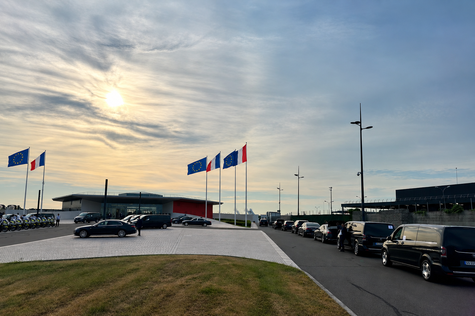 Flotte de véhicules Francelimo alignée devant un bâtiment institutionnel pavoisé de drapeaux européens et français, au lever du jour