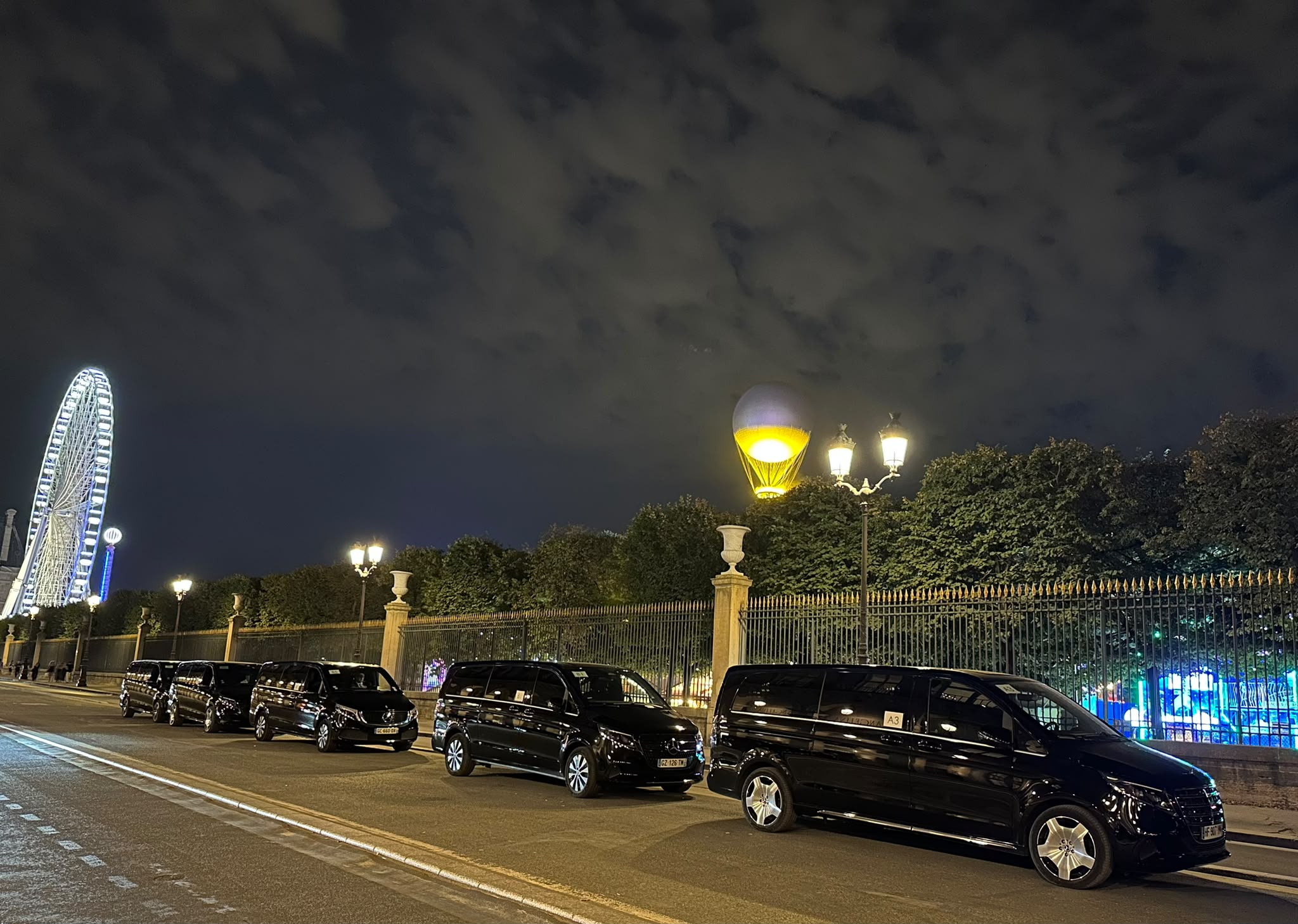 Flotte de vans Francelimo alignée de nuit au bord du jardin des Tuileries, grande roue en arrière-plan